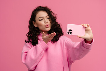 Wall Mural - happy smiling woman in pink hoodie posing on pink studio background holding smartphone