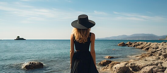 Poster - Serene Woman in Black Dress With Hat on Rocky Cliff Overlooking Ocean