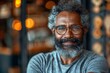 A cheerful elderly man with a full beard and spectacles smiling warmly in a cozy indoor setting with bokeh lights