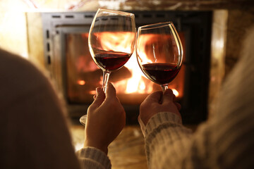 Wall Mural - Couple clinking glasses of wine near fireplace at home, closeup