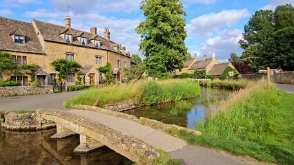 Wall Mural - Calm Cotwolds village of Lower Slaughter with reflections in rippling water of the River Eye, Gloucestershire, England. Handheld panning motion.