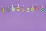 Fototapeta Lawenda - Easter template with garland and space for text. Decorative Easter eggs on a rope on a purple background. Greeting card or banner
