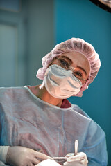 Wall Mural - Close up portrait of young female surgeon doctor wearing protective mask and hat during the operation. Healthcare, medical education, surgery concept