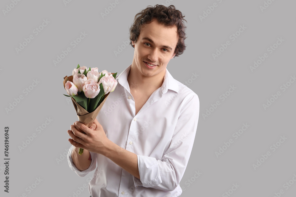 Young man with bouquet of tulips on grey background