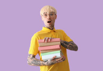 Wall Mural - Shocked tattooed young man with stack of books on lilac background