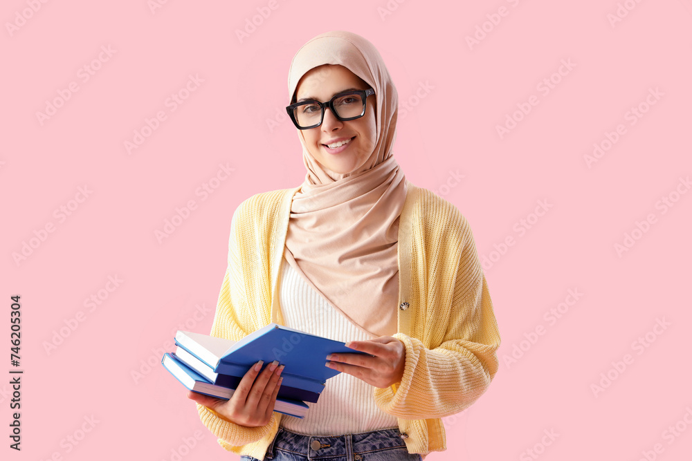 Young Muslim woman with books on pink background