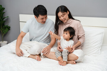 Wall Mural - happy family, mother and father with toddler baby on bed