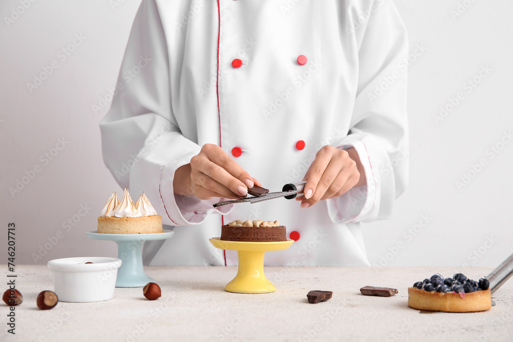 Female confectioner decorating tasty cakes on white background