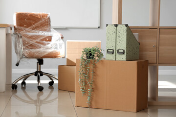 Poster - Interior of light office with chair wrapped in stretch film and cardboard boxes on moving day