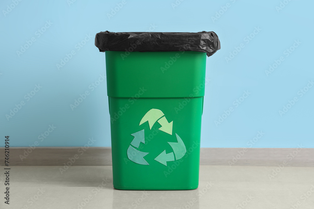 Empty trash bin with recycle logo near blue wall