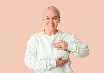 Wall Mural - Mature woman checking her breast on beige background. Cancer awareness concept