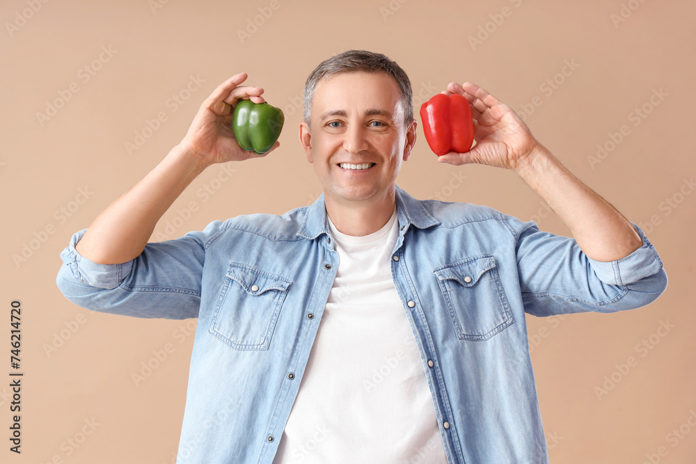 Mature man with bell peppers on beige background