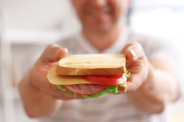 Canvas Print - Middle-aged man with delicious sandwich made from crispy toasts in kitchen, closeup