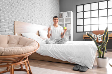 Sticker - Young man with pillbox and pills sitting on bed in bedroom