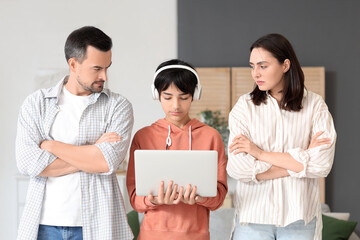 Wall Mural - Teenage boy in headphones with laptop and his upset parents at home. Family problem concept