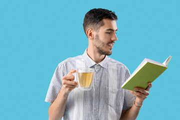 Poster - Young man with cup of tea and book on blue background