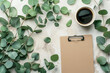 Flat lay composition with a cup of coffee, fresh eucalyptus branches, and a clipboard on a beige background, suitable for minimalistic design concepts or creative workspace themes