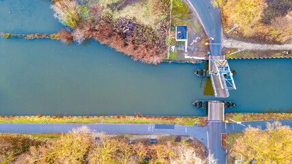 This aerial image provides a top-down view of a canal lock system, where the calm waters are managed for navigational purposes. The lock, a feat of engineering, sits at the juncture where two roads