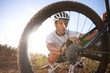 Checking, man and bicycle chain by wheel, nature and mountain biking in countryside. Male person, workout and lens flare for fitness or exercise, hobby and sports for adventure and tyre inspection