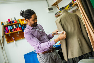 Male African American tailor measuring the suit with measuring tape.