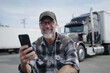 Happy truck driver using cell phone on parking lot and looking at camera