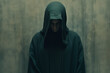 A dark cloaked figure, a man with a hood on standing in front of a wall, wearing a dark robe.