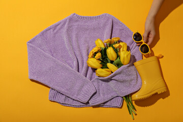 Wall Mural - Sweater, flowers, rubber boots and glasses in hand on yellow background, top view