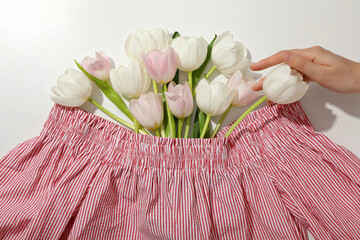 Wall Mural - Female blouse, tulips and hand on white background, top view