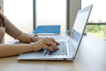 Closeup businesswoman hand typing on laptop computer keyboard. Working atmosphere in modern office with large glass window. Side view