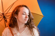 Portrait of a pensive pretty girl under a yellow umbrella in front of a dark blue background