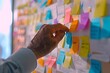 An elderly man stands in an office surrounded by soft vibrant post it notes stuck to the wall and his hand He is using collaborative techniques to plan and document ideas for the workplace