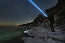 A Man With A Flashlight Walking On The Steep Shore Of The Baltic Sea In Paldiski At Night In Winter Time.