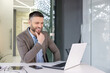 © Liubomir - Smiling businessman in office using laptop with phone and tablet on desk