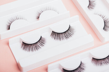 Different fake eyelashes in boxes on trendy pastel pink background. Makeup accessories and beauty cosmetics products for women. Top view, flat lay.