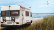 Wohnmobil parkt am Strand mit Meerblick, Surfer und Dünengras, Camping am Meer