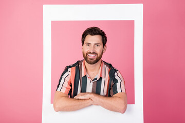 Poster - Photo of handsome man with bristle folded hands inside paper frame shooting his white teeth smile isolated on pink color background