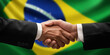 Businessman and diplomat in suits clasp hands for handshake over Brazil flag, agree on united success in trade, diplomacy, cooperation, negotiation, support, teamwork in commerce, gesture of greeting