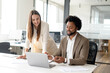 © Vadim Pastuh - A businesswoman leans over to discuss a point on a laptop with her male colleague, reflecting a collaborative effort in a corporate setting. Diverse work team concept