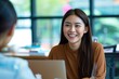 © shelbys - Smiling woman sitting at a table with a laptop, engaging in a conversation or working