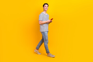 Sticker - Full size photo of optimistic student dressed striped t-shirt hold smartphone go to empty space isolated on yellow color background