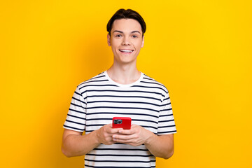 Canvas Print - Photo of intelligent guy with stylish hairdo dressed striped t-shirt holding smartphone read news isolated on yellow color background