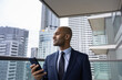 © ReeldealHD images - Businessman on office balcony using smartphone and looking at city skyline