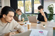 © LIGHTFIELD STUDIOS - Young professionals deeply focused while working on laptops in a coworking space, blurred foreground