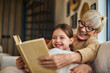 © bnenin - A lovely smiling grandma and her grandchild, reading a book together, sitting on the couch.