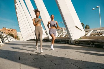 Two young women in sportswear are running on modern buildings background. Active lifestyle concept