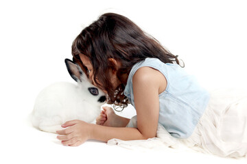 Wall Mural - Cute little girl kissing rabbit while lying on floor. Joyful kid with her pet on white background. Happy child playing with her cute bunny. Children gently take care for pets with love.