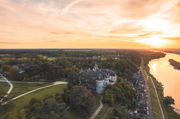 Wall Mural - A magnificent castle stands proudly nestled by a winding river, illuminated by the golden hues of the setting sun. The tranquil waters reflect the beauty of the ancient architecture