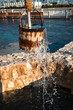 Closeup of flowing water at old well fountain, famous place in the middle of Souq Waqif, Doha center, Qatar. Middle East, Arabian Peninsula. Doha Mosque with minaret on blurred background. Blue sky.