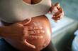© Davor - Young woman applying stretch mark cream to pregnant belly at home