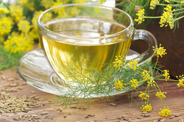 Canvas Print - Fennel seed tea or extract on wooden background with fresh flowers nearby, copy space, natural medicine, drink for breast milk production, sleep and stress care tea concept